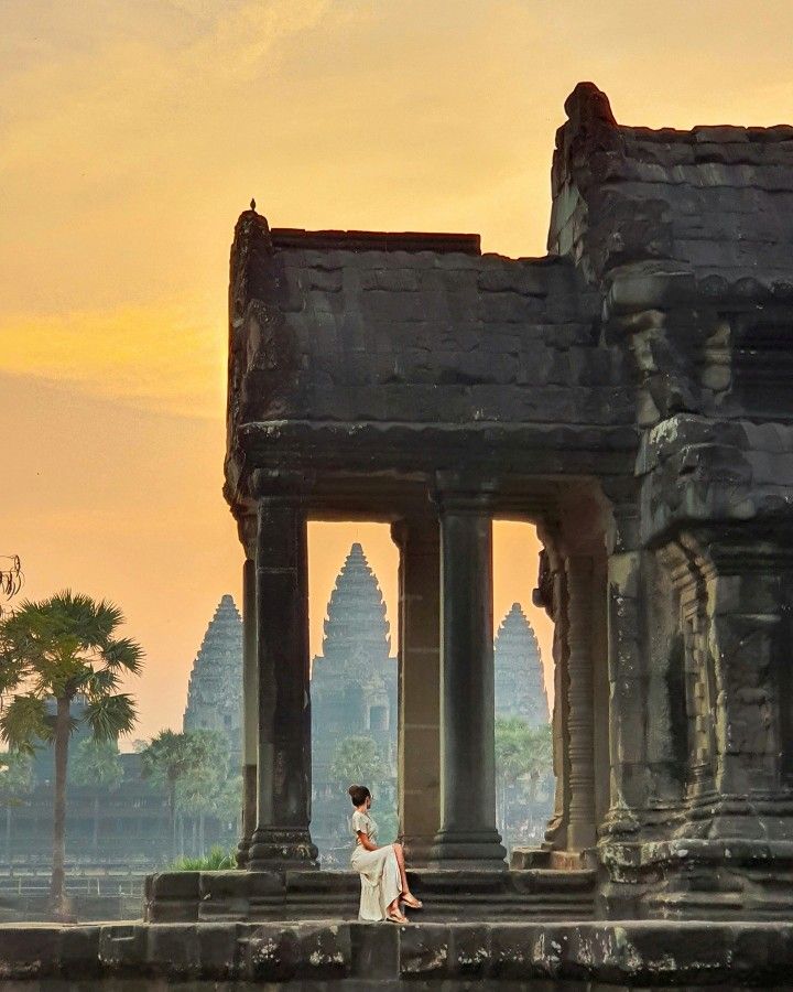 a woman standing in front of an old building with columns and arches at sunset or dawn