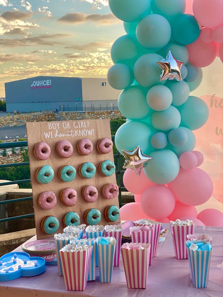 a table topped with donuts and cupcakes next to a giant balloon arch