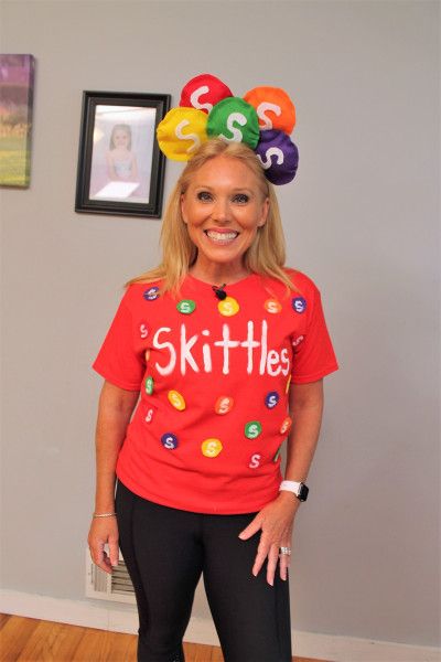 a woman wearing a red shirt with the words skittles on it and balloons above her head