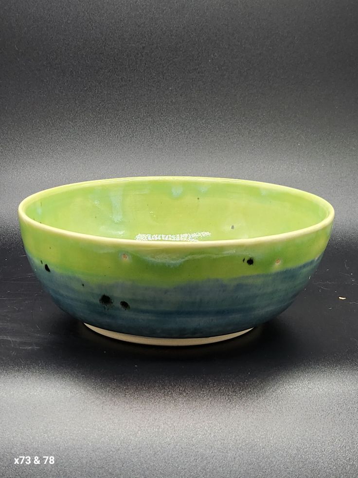 a green and blue bowl sitting on top of a table next to a gray wall