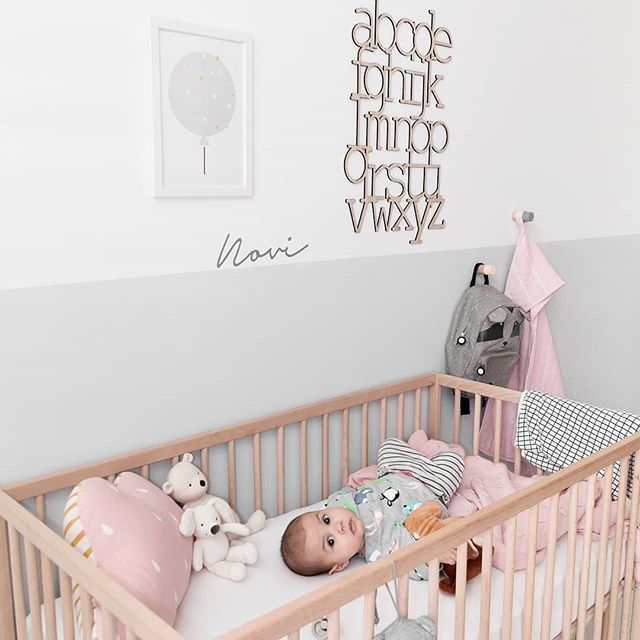 a baby in a crib with stuffed animals on the floor and wall behind it