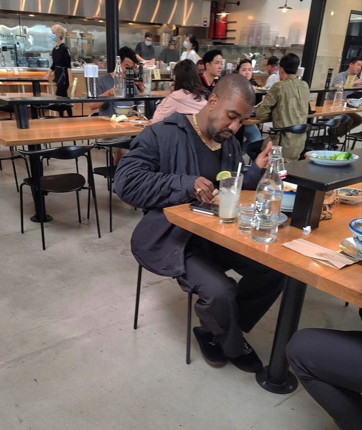 a man sitting at a table in a restaurant with plates and glasses on it while looking at his cell phone