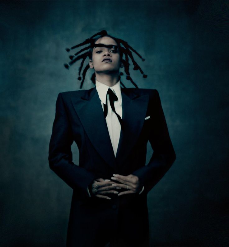 a man in a suit and tie with dreadlocks on his head, standing against a dark background