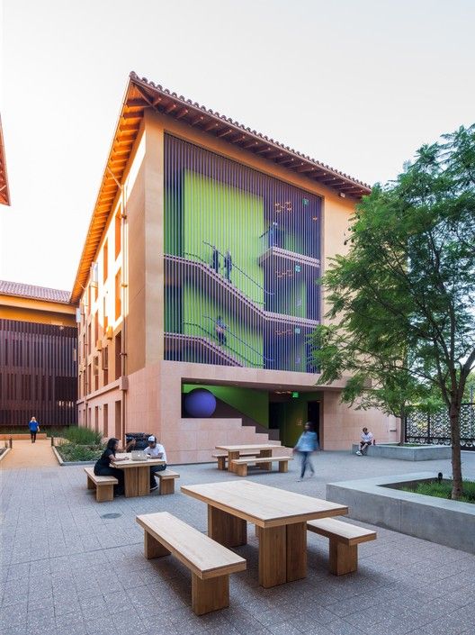 people are sitting at picnic tables in front of a building with stairs on the side