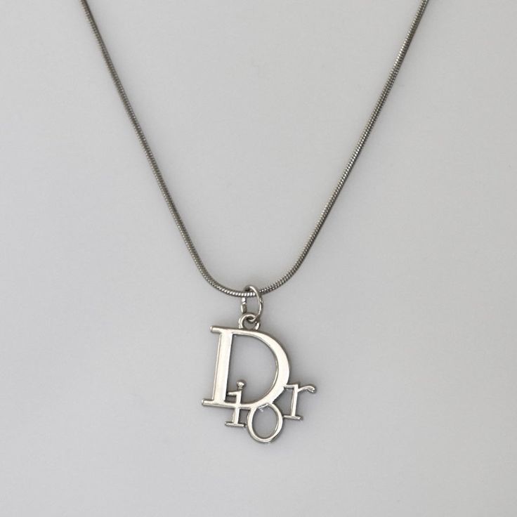 Authentic Christian Dior logo pendant set on a stainless steel 18 inch chain. Luxury Silver Jewelry With Silver-tone Logo, Affordable Classic Silver Charm Necklaces, Christian Dior Jewelry Vintage, Saint Laurent Necklace Silver, Silver Charm Necklace With Logo As Gift, Silver Metal Snake Chain Charm Necklace, Silver Charm Necklaces With Snake Chain, Luxury Silver Charm Necklace With Round Pendant, Vintage Silver Necklace With Logo Charm