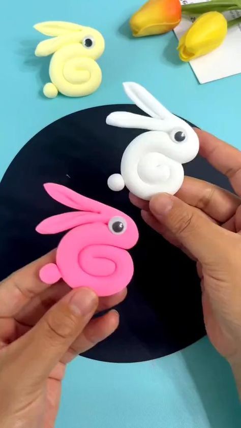 someone is making some bunny decorations out of plastic material on a blue table with yellow and pink flowers