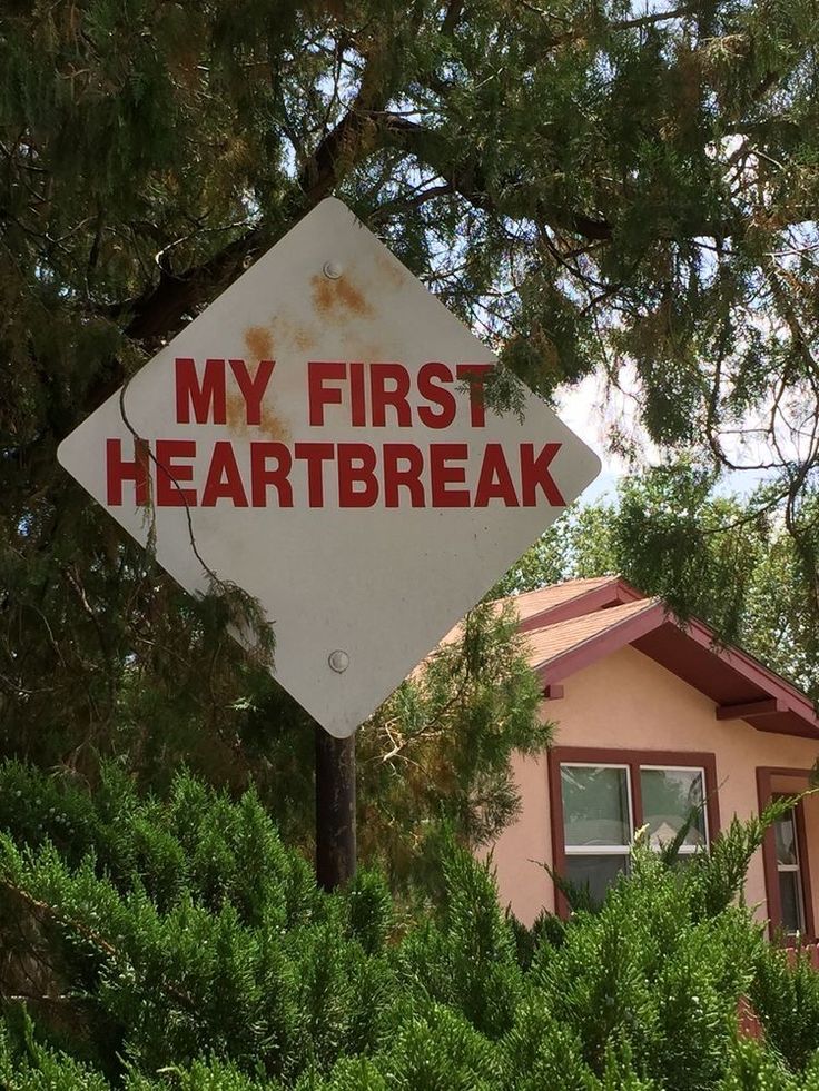 a red and white sign that says my first heart break hanging from the side of a tree