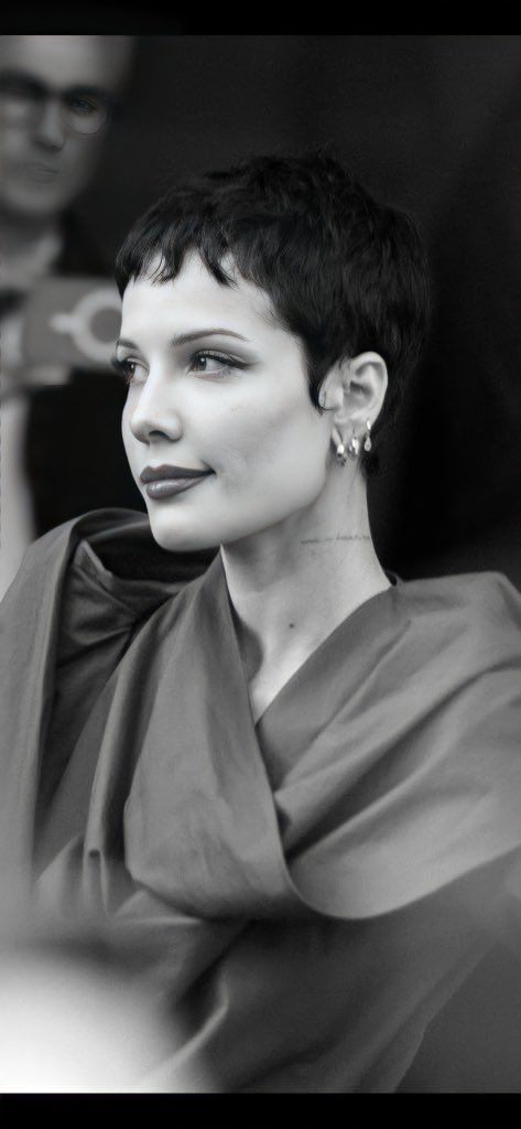 a black and white photo of a woman with short hair wearing a gray dress looking off to the side