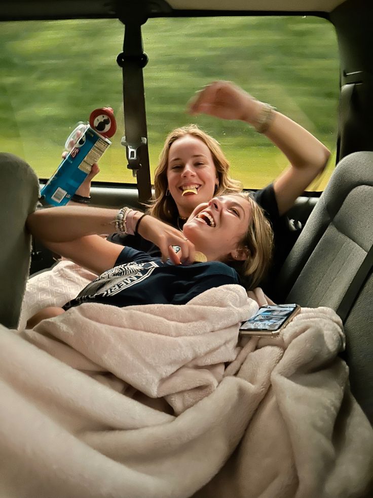 two women are laying in the back of a car and one is holding a toothbrush