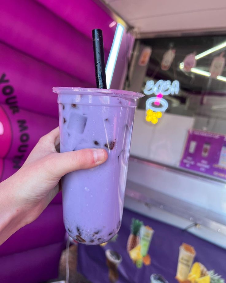 a person holding up a purple drink in front of a building