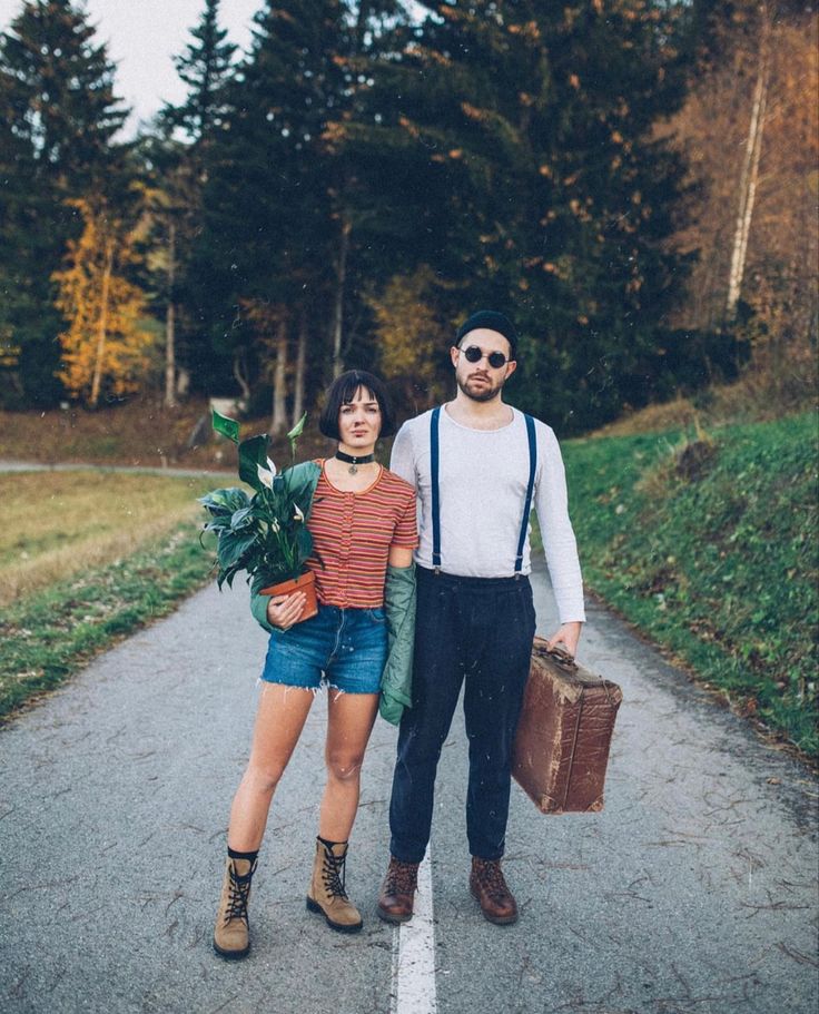 a man and woman standing on the side of a road with luggage in their hands