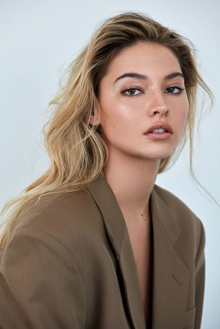 a woman with long blonde hair wearing a brown blazer and looking off to the side