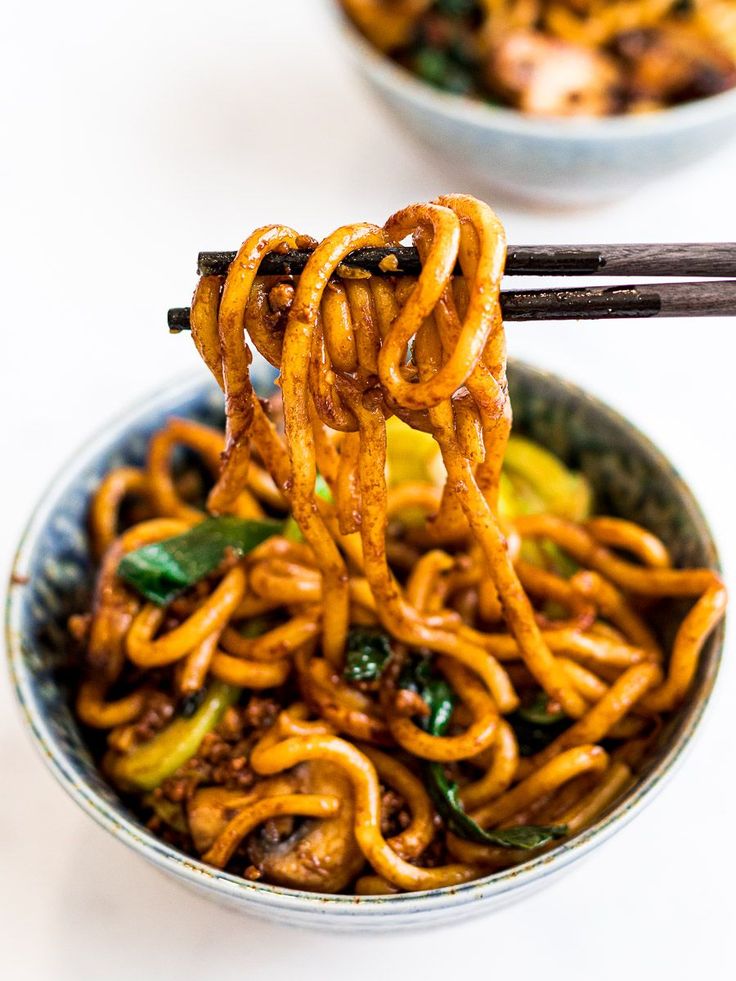 noodles being lifted from a bowl with chopsticks over them and another bowl in the background