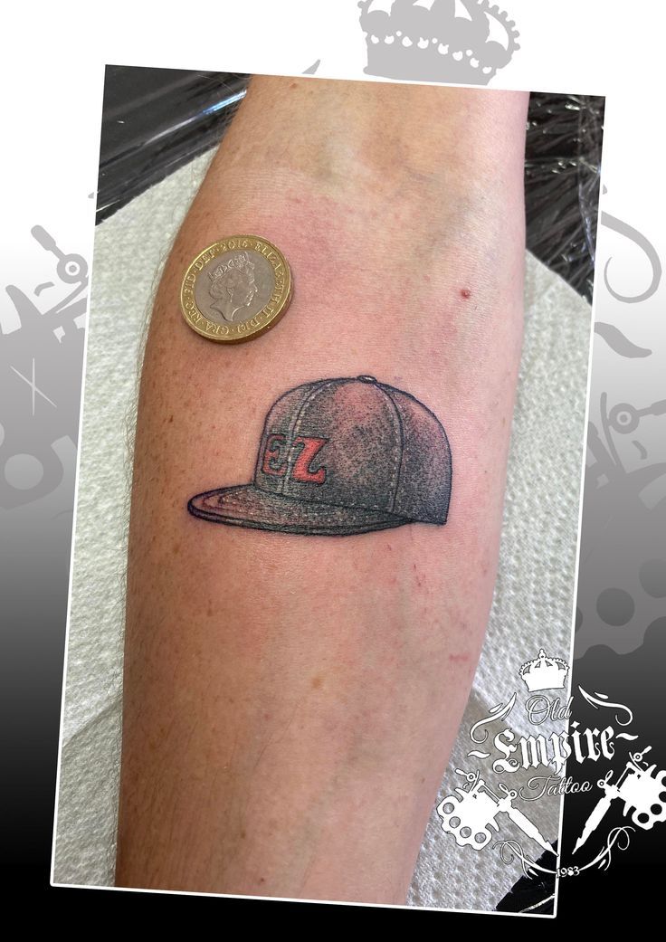 a man's arm with a baseball cap on it and a coin sitting next to it