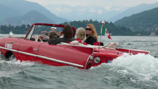 people are riding in a red convertible boat on the water with mountains in the background