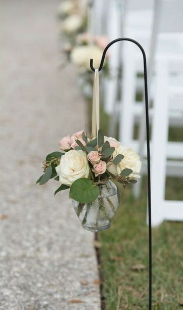 a vase with flowers and greenery on the side of a road next to white chairs