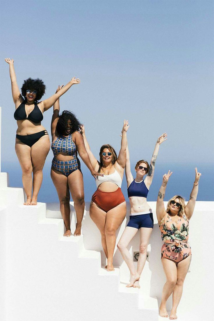 four women in bikinis are standing on the edge of a white wall and reaching up into the air