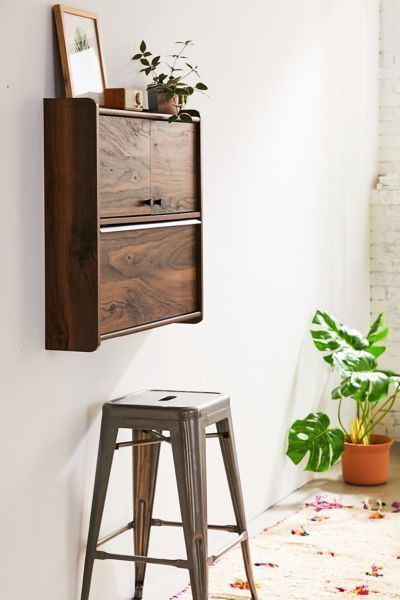 a tall wooden cabinet sitting next to a metal stool and potted plant on top of a white wall