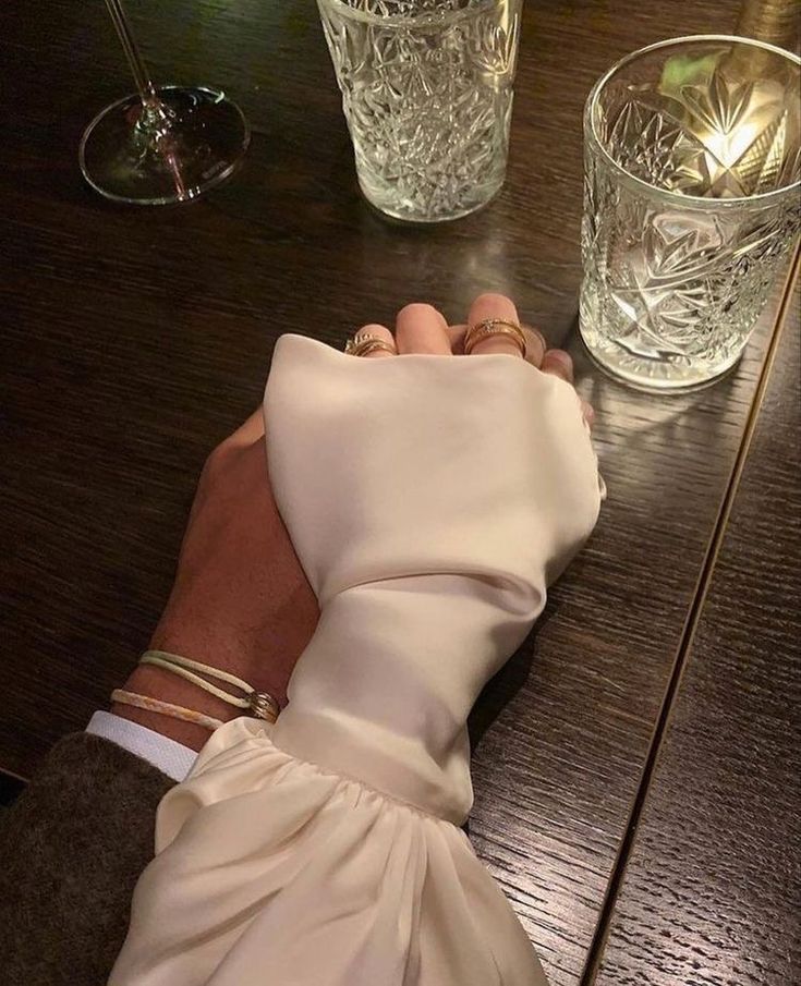 a woman's hand holding onto a napkin on top of a wooden table next to two glasses