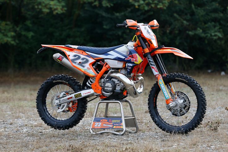 an orange and white dirt bike parked on top of a metal stand in the grass