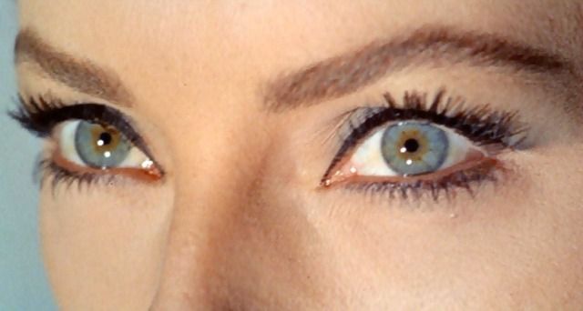 a woman's blue eyes with long lashes and brown eyebrows are seen in this image