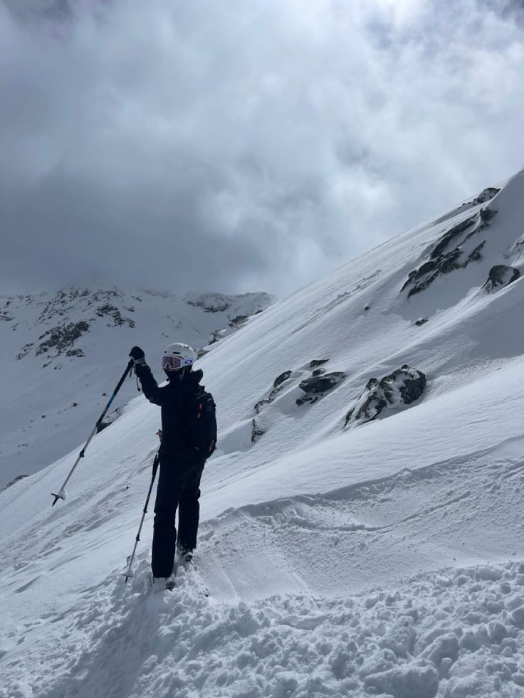 a man standing on top of a snow covered slope holding ski poles in his hand