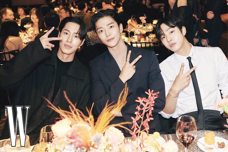 three men sitting at a table with food and drinks in front of them, posing for the camera