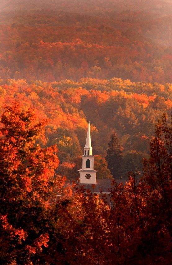 a church steeple surrounded by trees with fall foliage in the foreground and mountains in the background