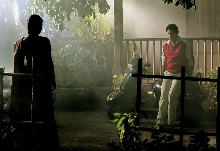 two people standing in front of a fence at night with the sun shining on them