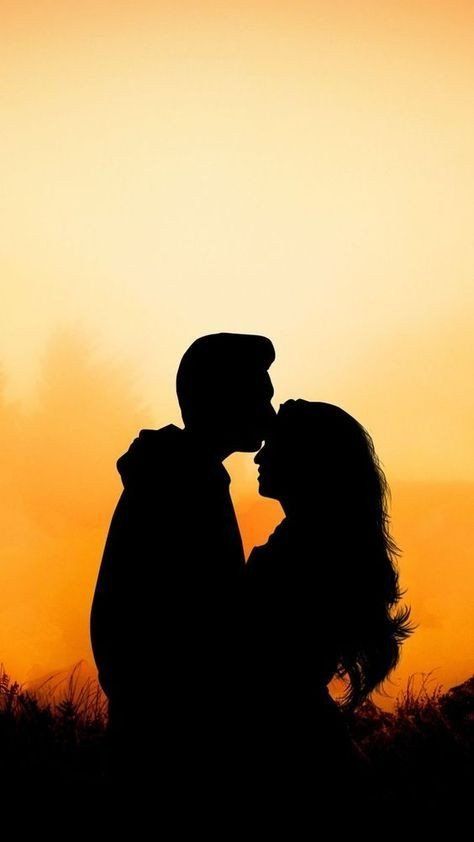 the silhouette of two people kissing in front of an orange sky