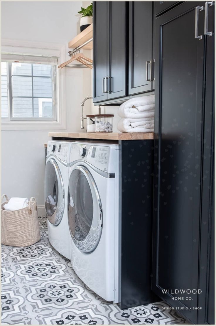 a washer and dryer in a small laundry room with black cabinets, white tile flooring and wooden shelves