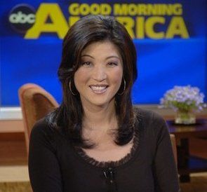 a woman sitting down in front of a news desk with a smile on her face