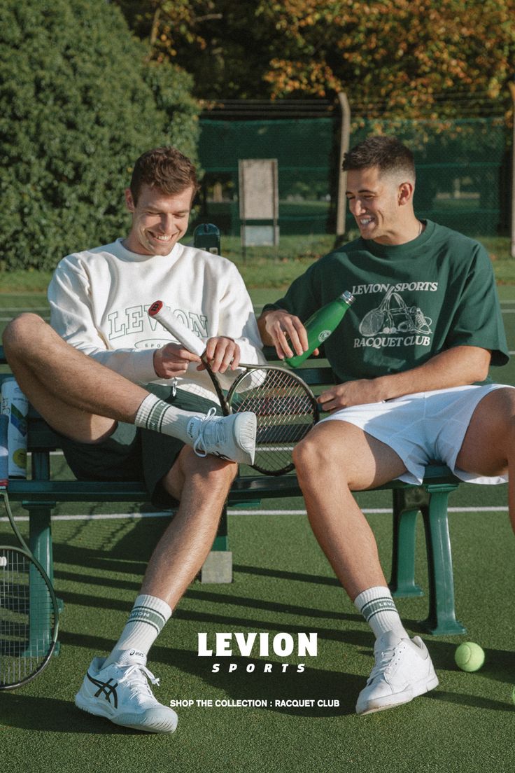 two men sitting on a bench holding tennis rackets