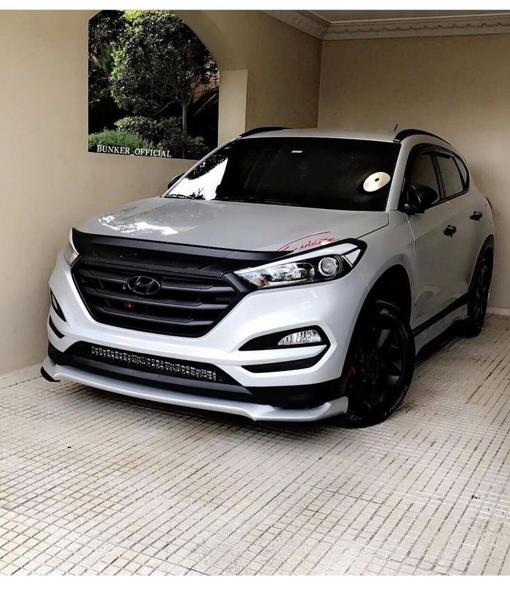 the front end of a white car parked in a garage next to a wall with an advertisement on it