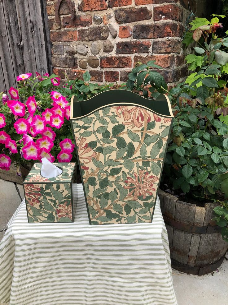 a chair and table with pink flowers in front of a brick wall on a patio