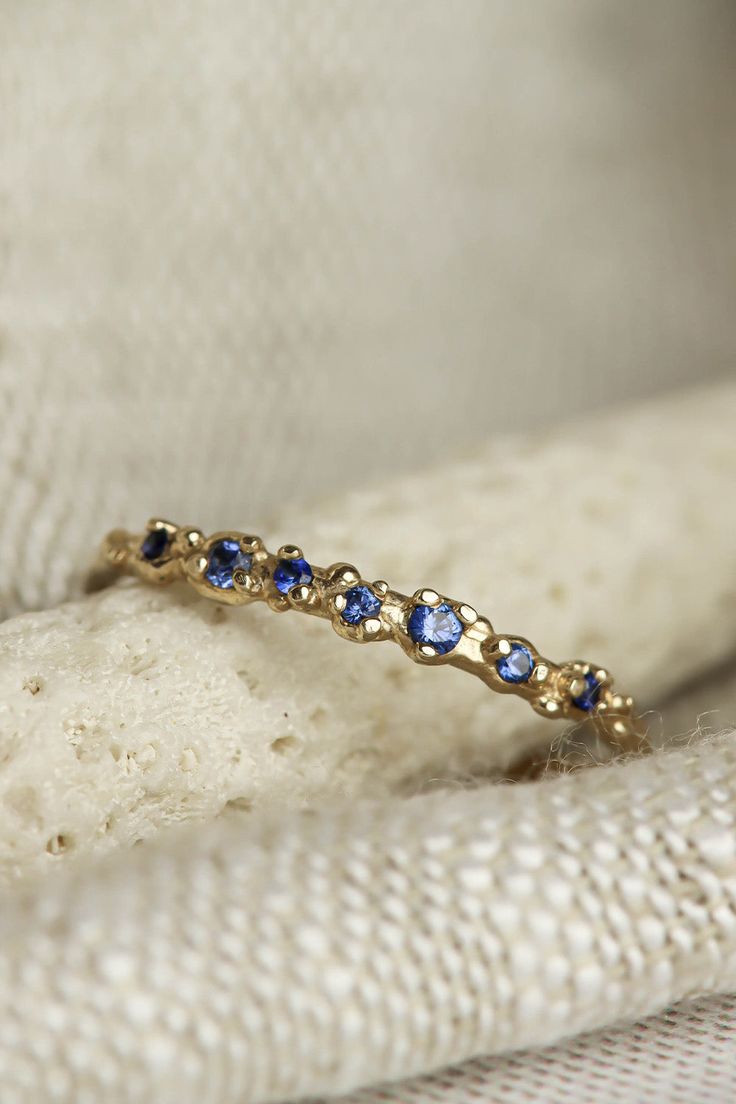 a gold ring with blue sapphires on it sitting on top of a white cloth