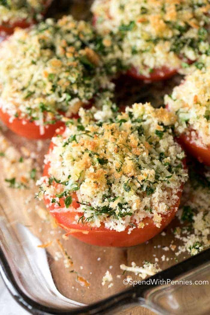 tomatoes stuffed with cheese and herbs in a glass dish on a wooden board, ready to be baked