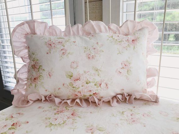 a bed with pink flowers and ruffles on the comforter is next to a window