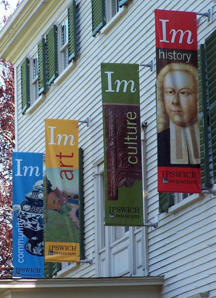 several banners hanging from the side of a white building with green shutters and windows