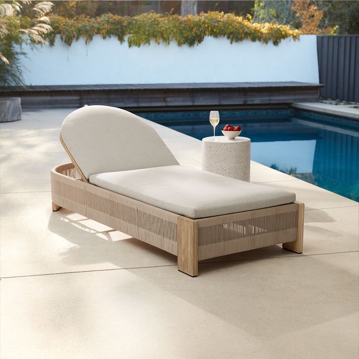 a chaise lounge next to a pool with a glass of wine on the table