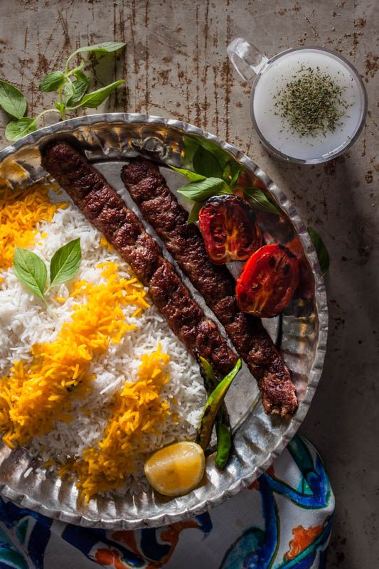 a plate with rice, meat and vegetables on it next to a bowl of seasoning