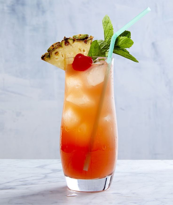 a drink with pineapple and mint garnish in a tall glass on a marble table