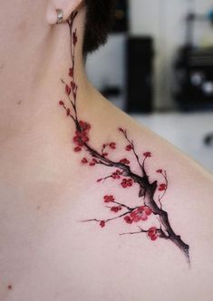 the back of a woman's shoulder with red flowers on it and a branch