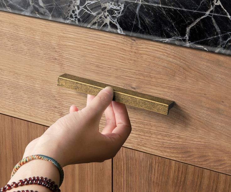 a person's hand reaching for a door handle on a wooden cabinet with marble top