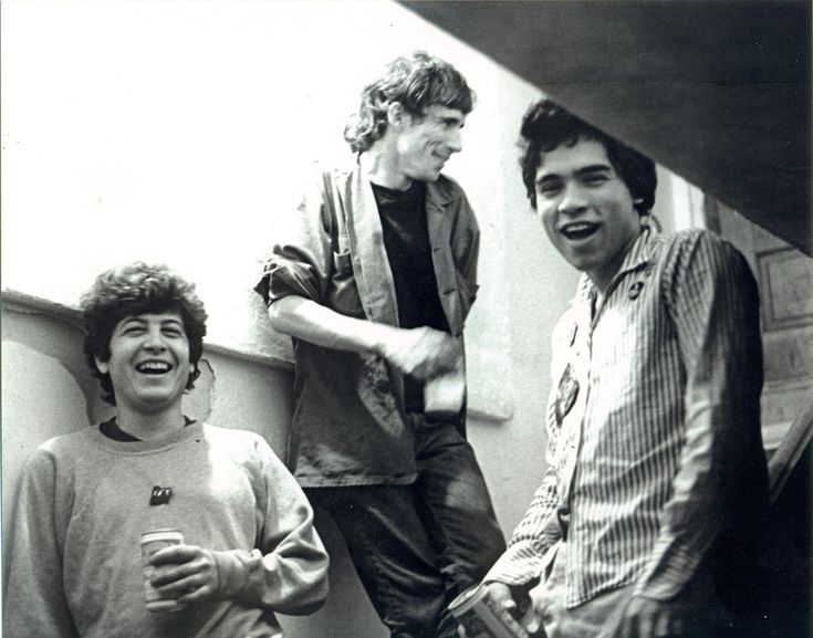 three young men standing next to each other on the side of a building, laughing