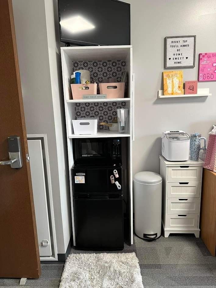 a room with a black refrigerator and some shelves on the wall next to a white rug