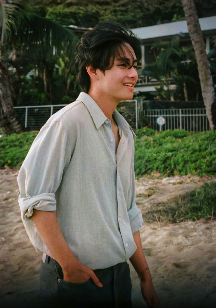 a young man standing on top of a sandy beach next to palm trees and buildings