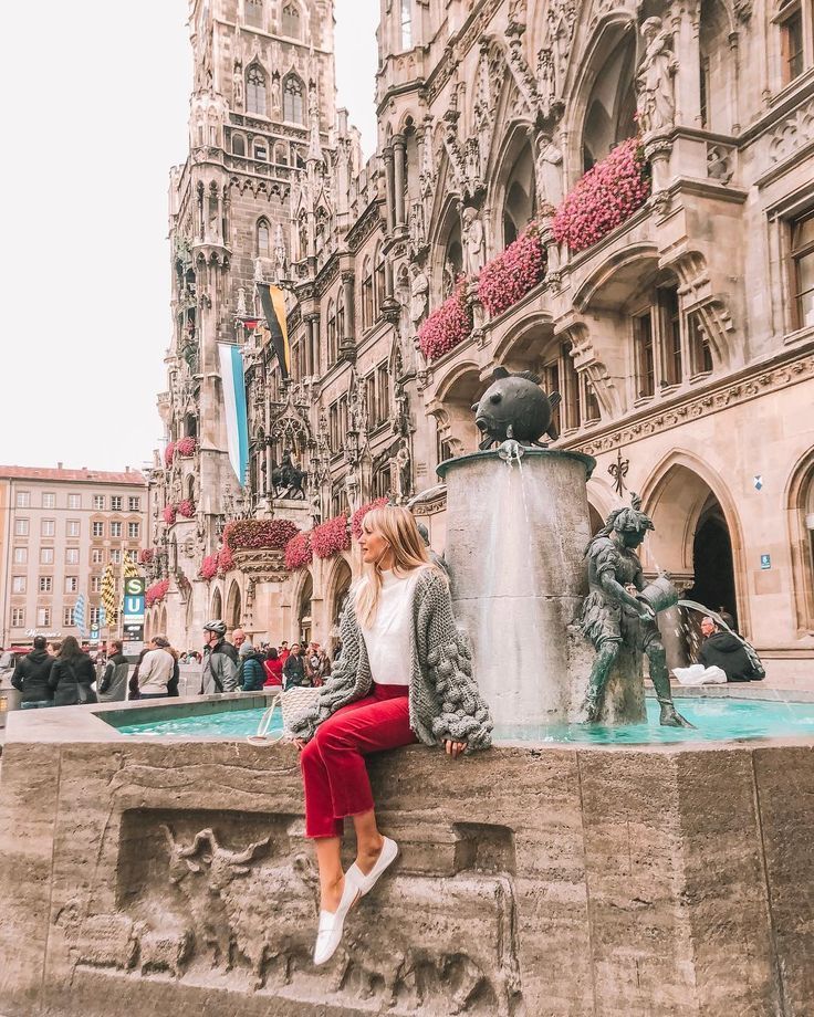 a woman sitting on the edge of a fountain in front of a building with statues