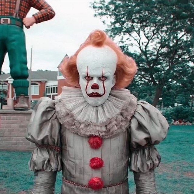 a creepy clown is standing in front of a man with a red nose and wig