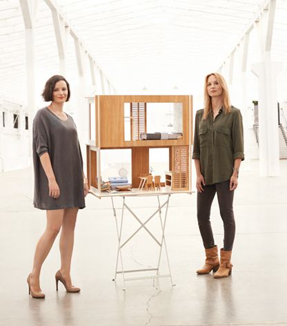 two women standing next to each other in front of a table with a house on it